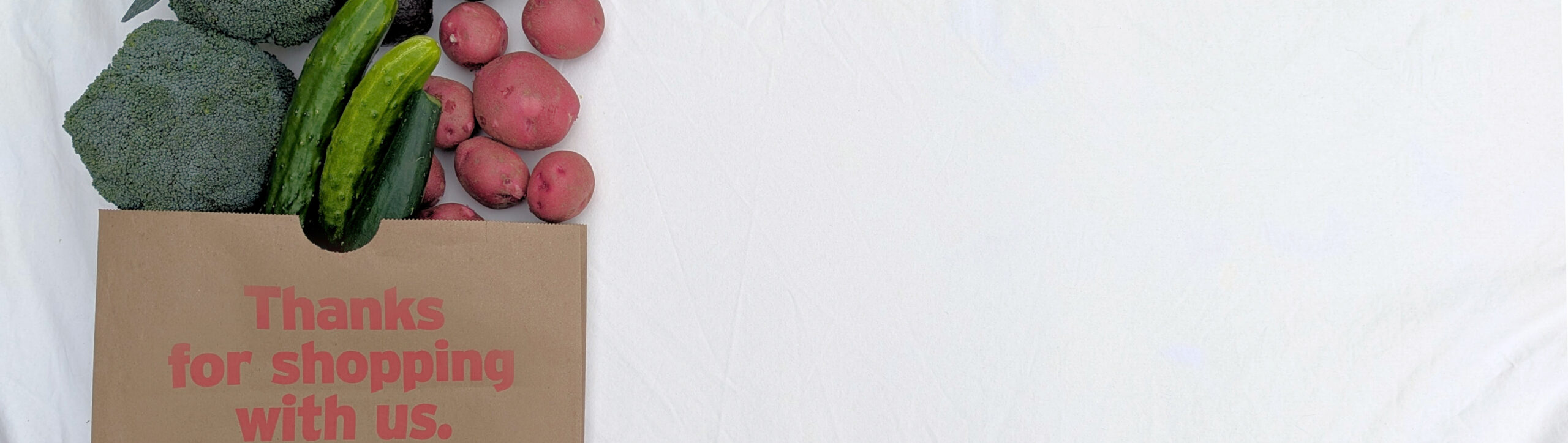 grocery bag with broccoli, cucumbers, potatoes